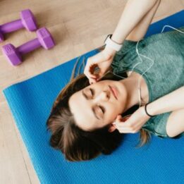 woman laid on fitness mat with weights wearing ear phones